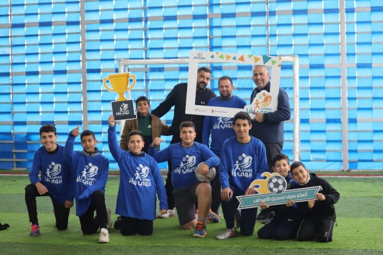 Boys in team shirts celebrating with a football trophy